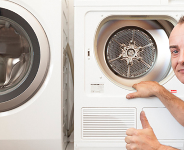 <p>Man geeft duim omhoog naast een wasmachine en droger.</p>