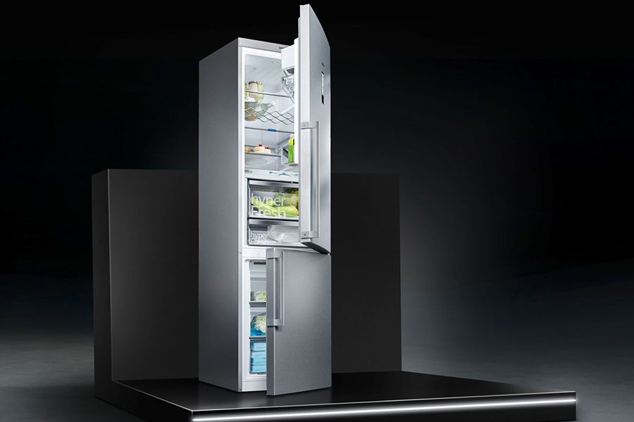 Een open, moderne zilverkleurige koelkast met twee deuren, waarvan de bovenste deur volledig geopend is en de onderste gedeeltelijk. De koelkast is gevuld met verschillende etenswaren.