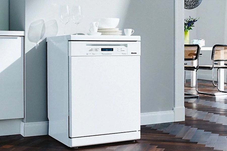 Witte afwasmachine in moderne keuken met servies erop.