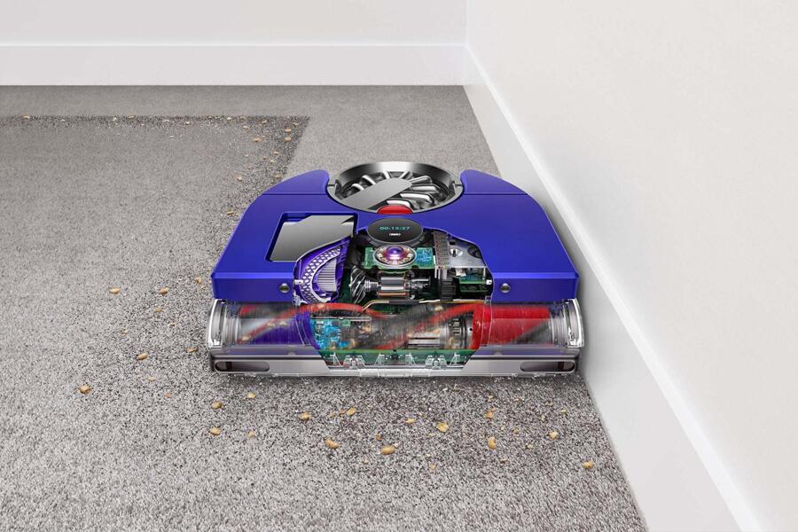 Een robotstofzuiger met zichtbare interne onderdelen die kruimels op een tapijt zuigt.