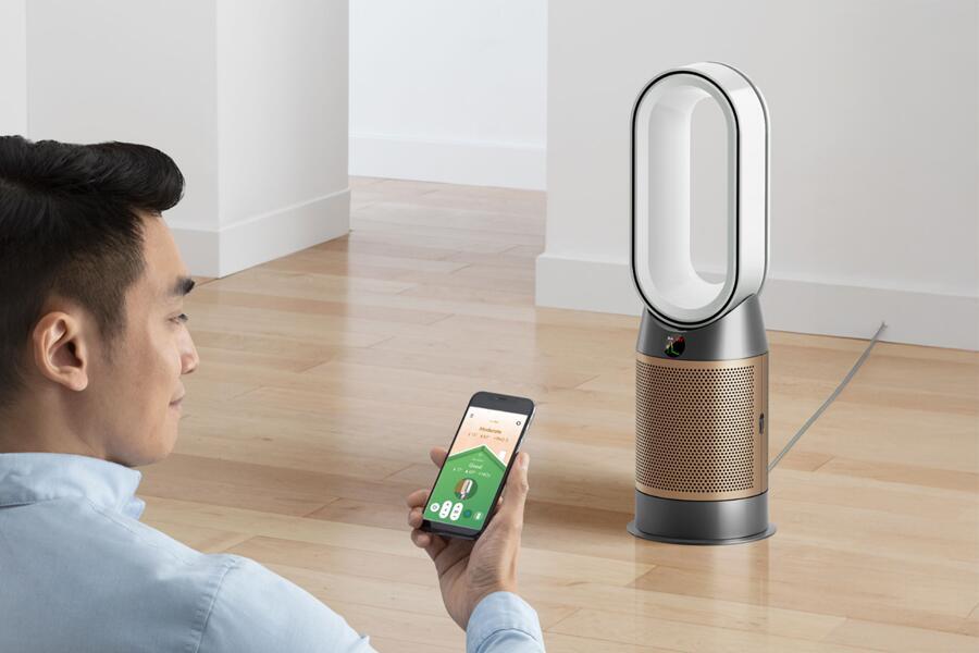 Man bedient een luchtzuiveraar met een smartphone in een lichte kamer.