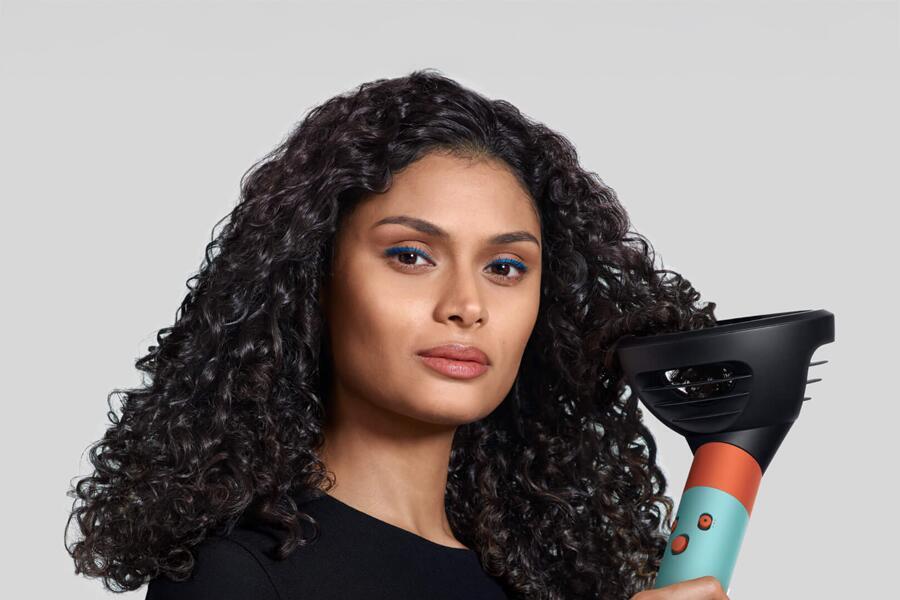 Een vrouw met krullend haar houdt een haarstyling apparaat vast.