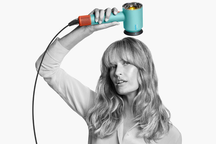 Vrouw houdt een kleurrijke föhn boven haar hoofd tegen een witte achtergrond.