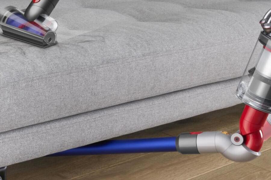 Stofzuiger met borstels reinigt grijze bank en vloer tegelijkertijd.